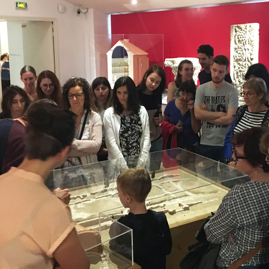 Un groupe, disposé autour d'une maquette, écoute le commentaire d'un guide.